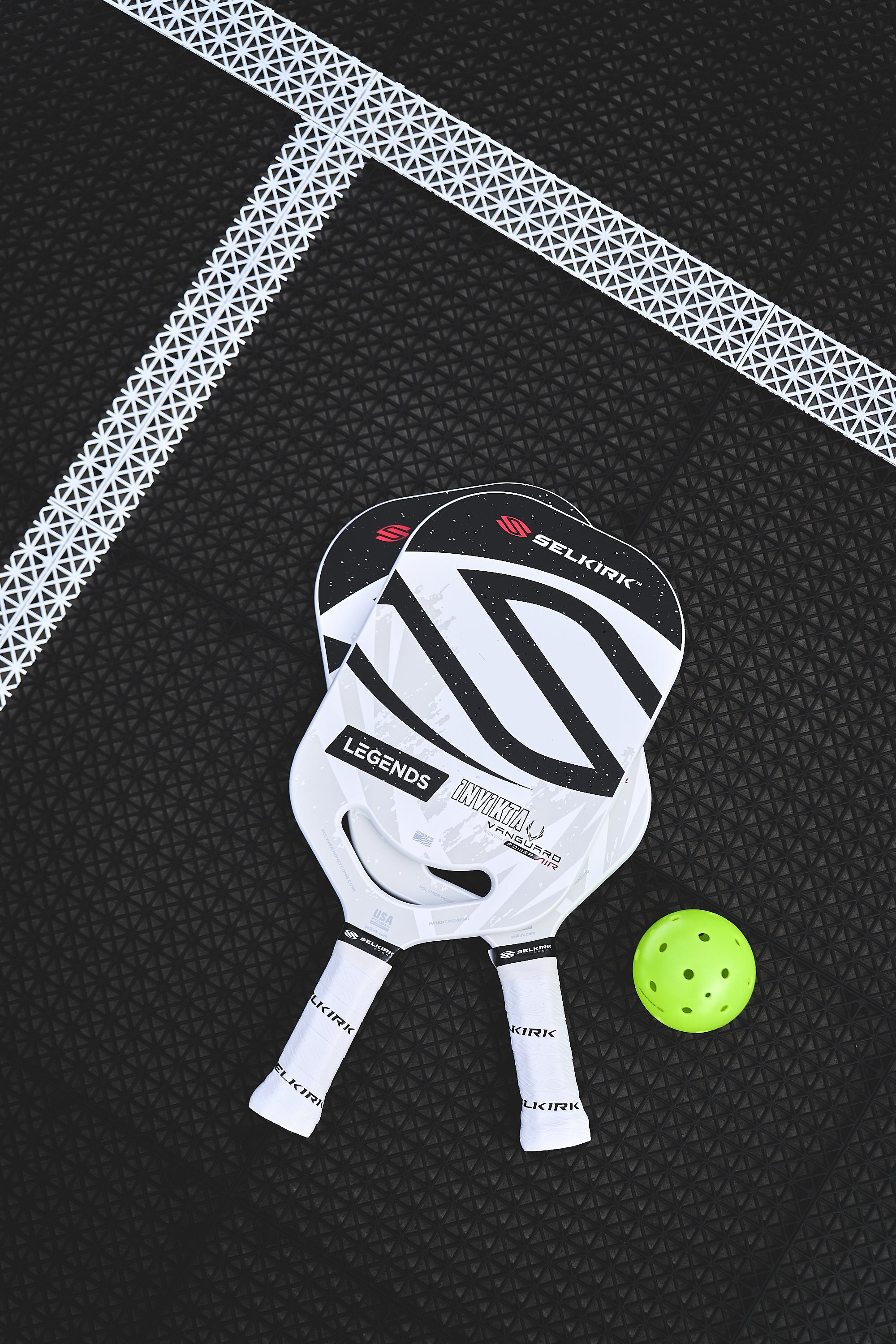 Two Selkirk pickleball paddles and a green ball on a court surface