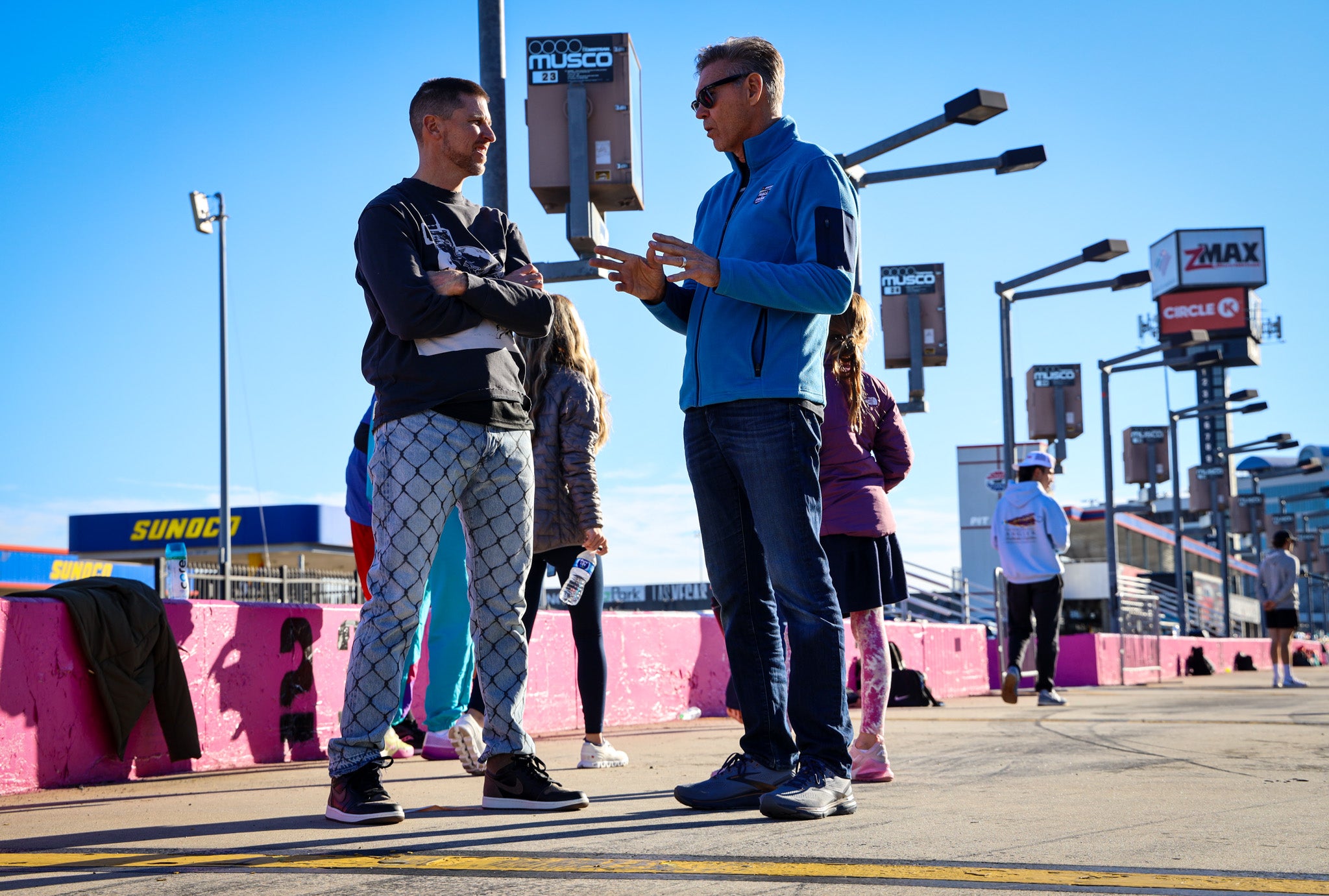 Austin Dillon and another man discussing at a NASCAR event with spectators in the background