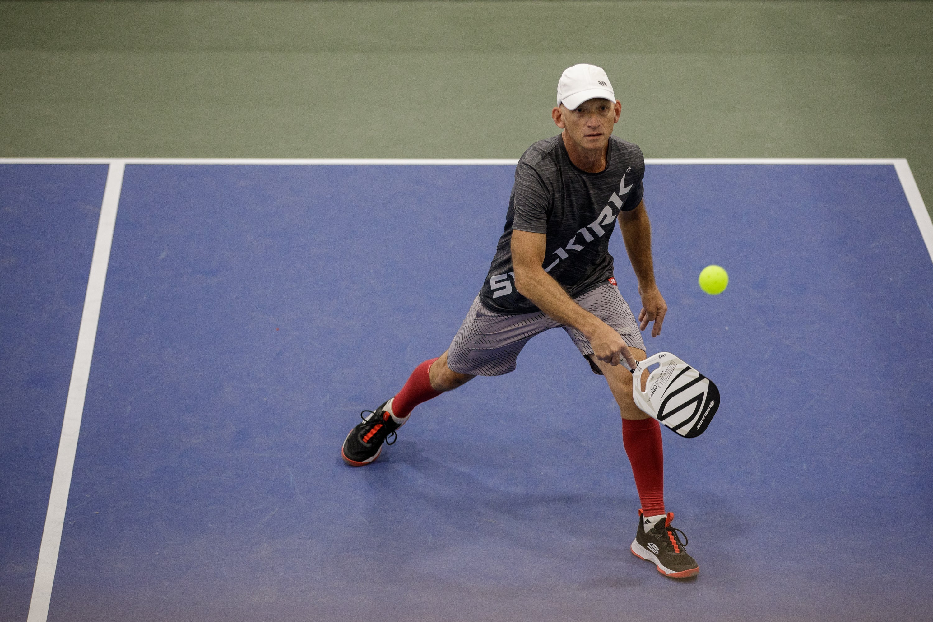 A player in a gray shirt and red leggings prepares to hit a pickleball during a game.
