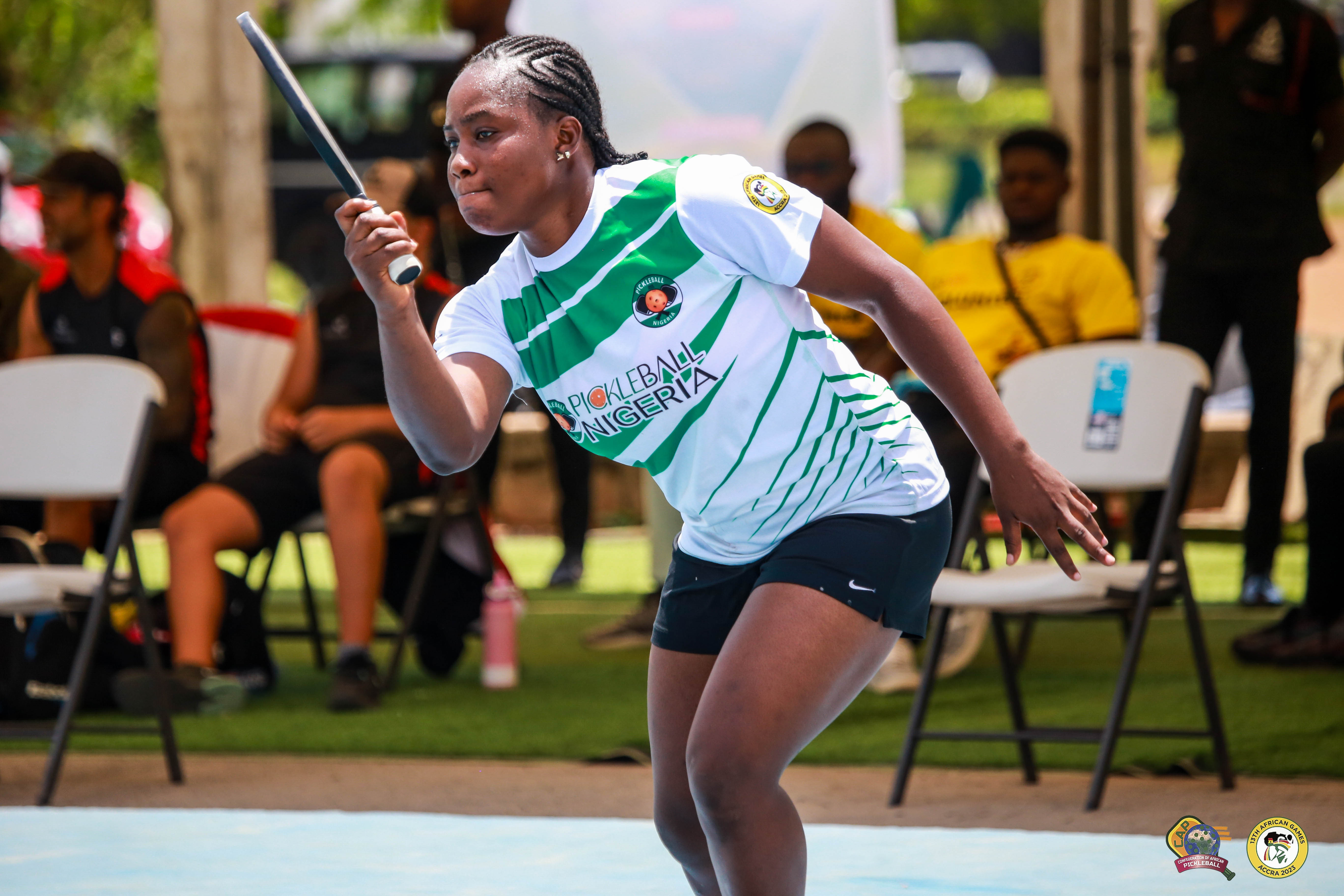 A woman competing in pickleball at the 13th African Games, wearing a green and white jersey.