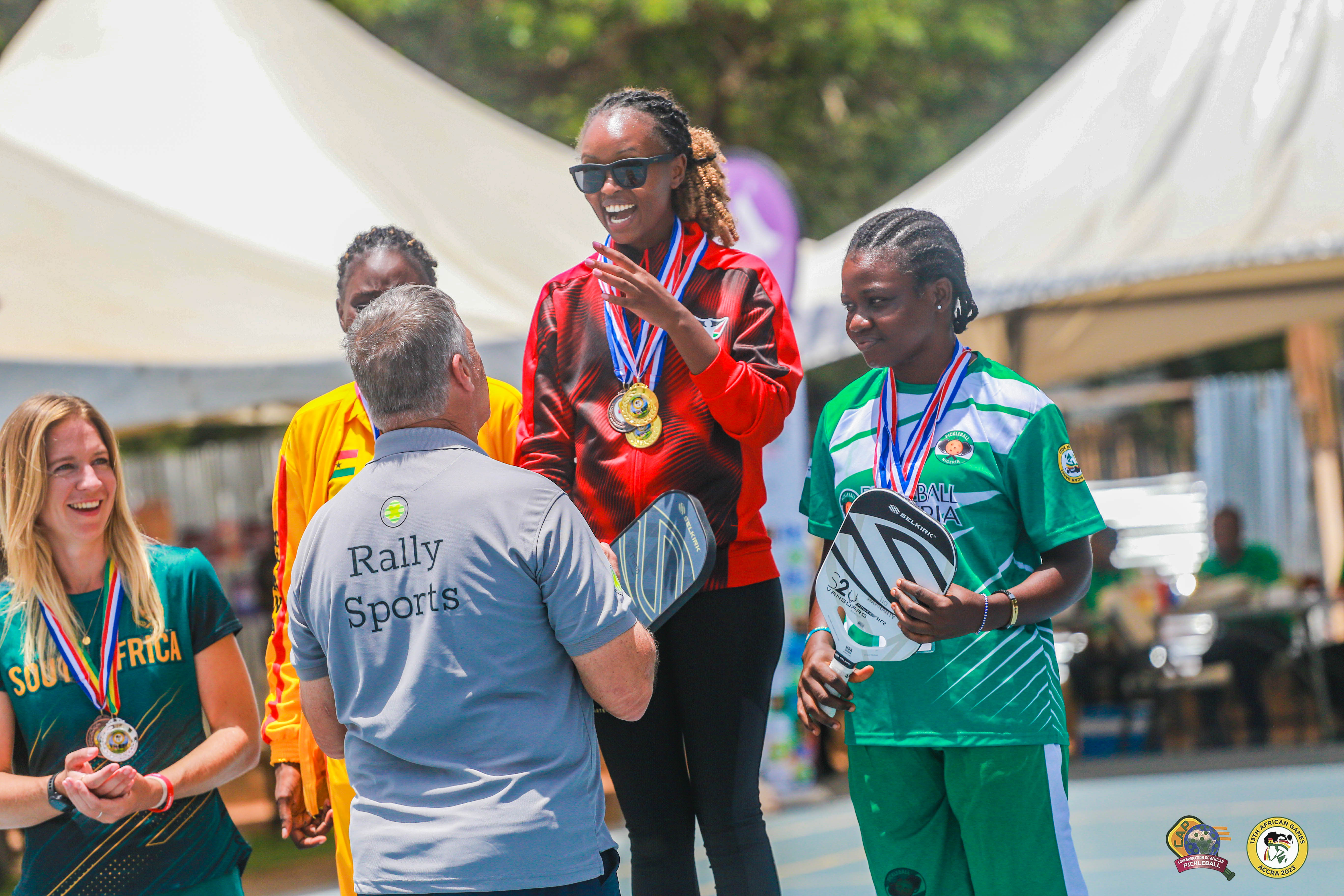 A woman receiving a medal at the 13th African Games, surrounded by competitors and officials.