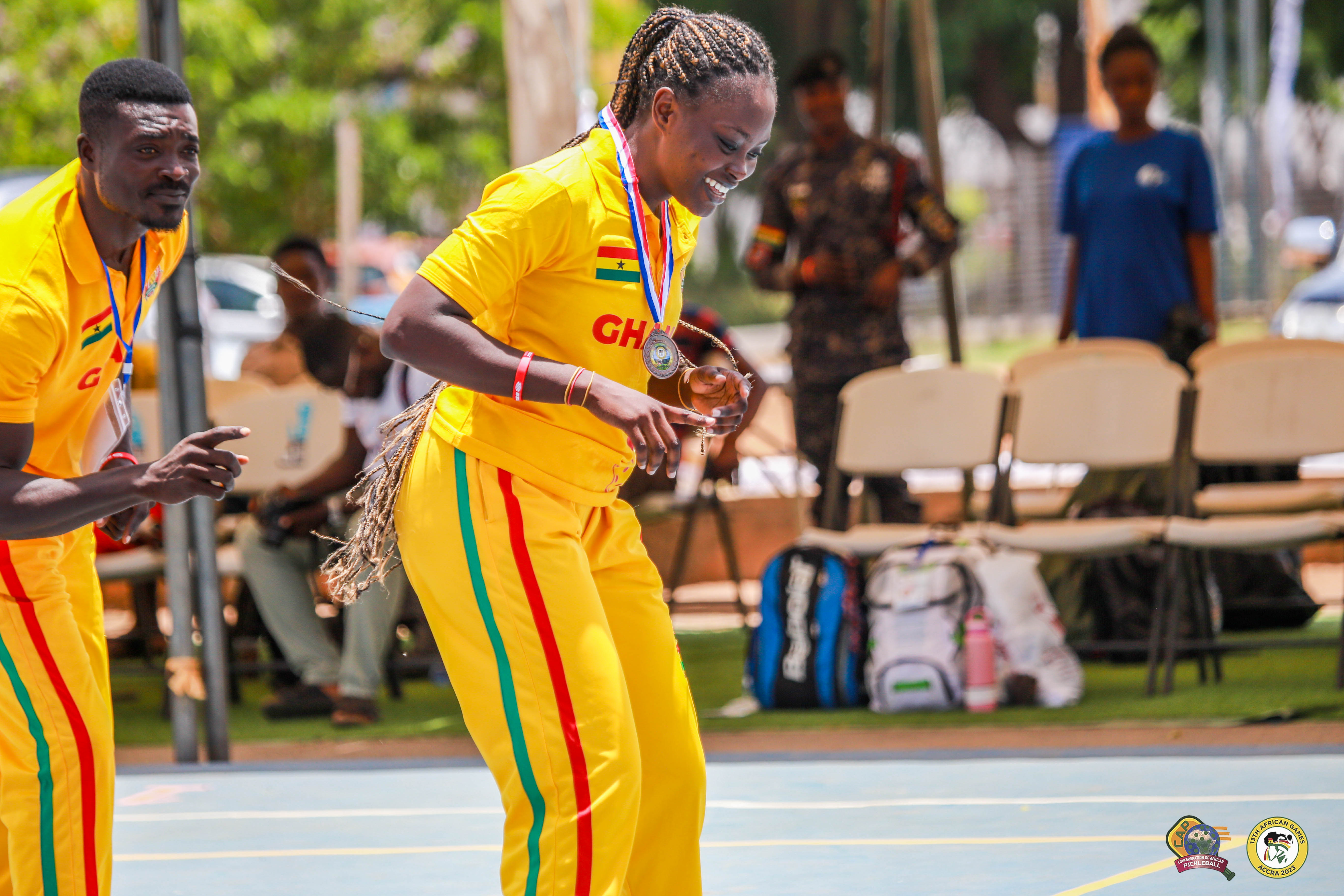 A woman in a yellow Ghana jersey smiles while competing in pickleball at the 13th African Games.