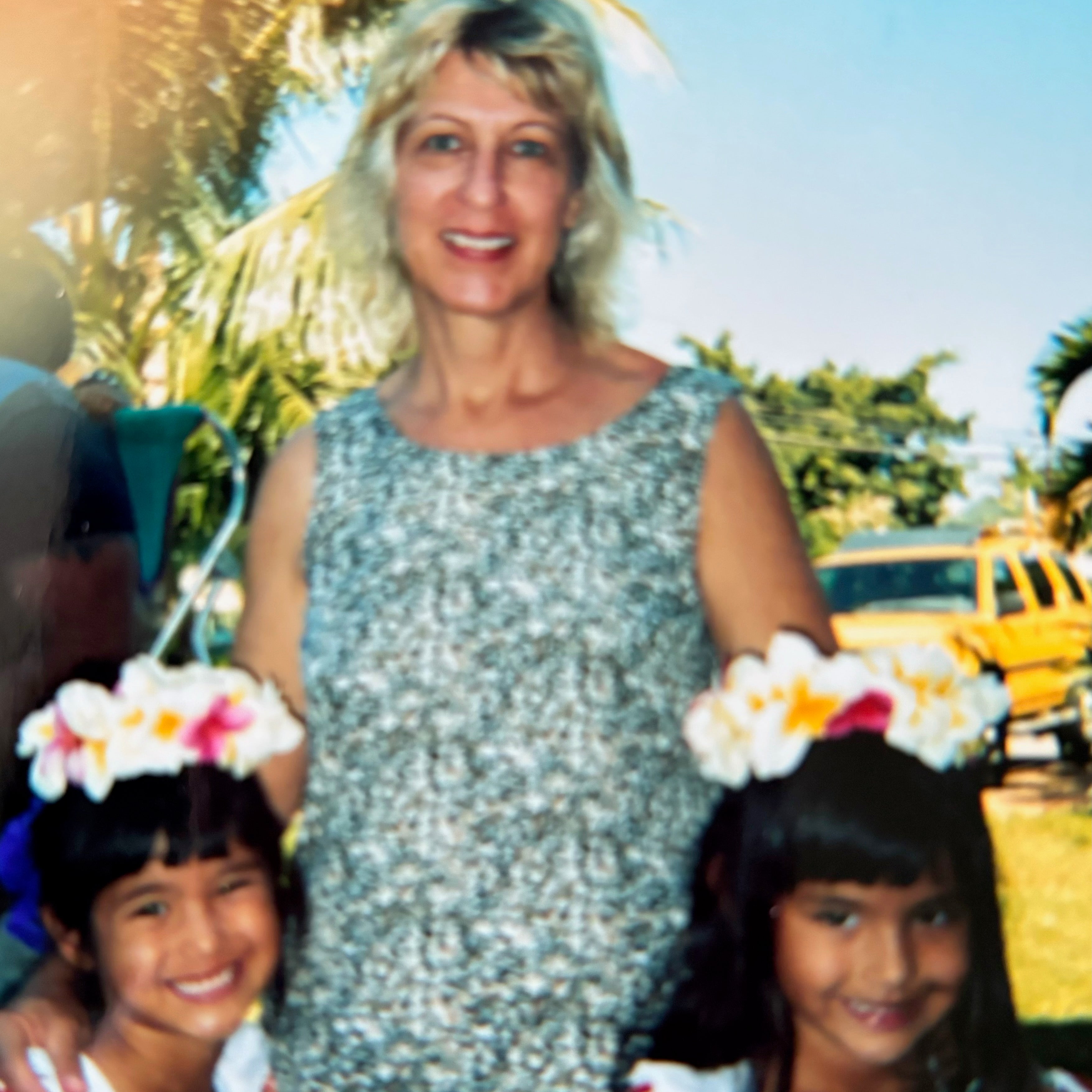 A mother with two daughters wearing flower crowns, smiling together outdoors.