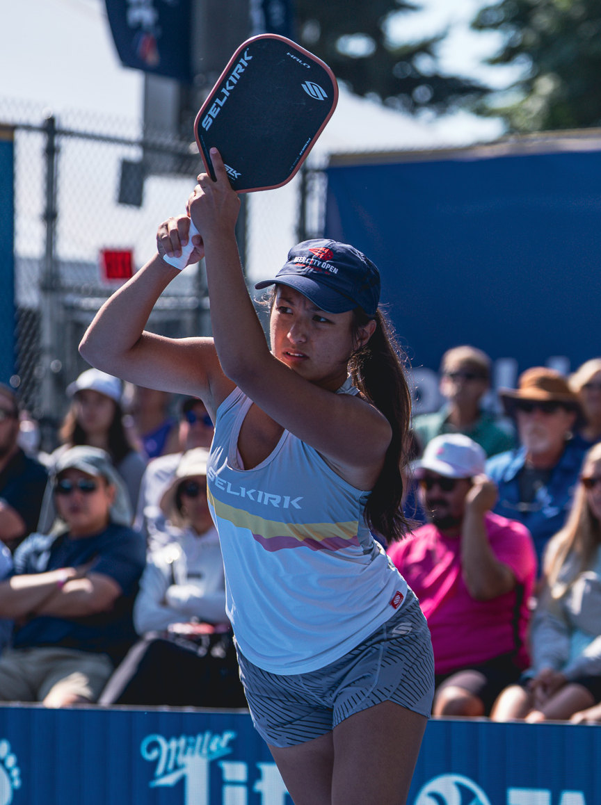 Jackie Kawamoto preparing to serve in a pickleball match, wearing a Selkirk shirt and cap.