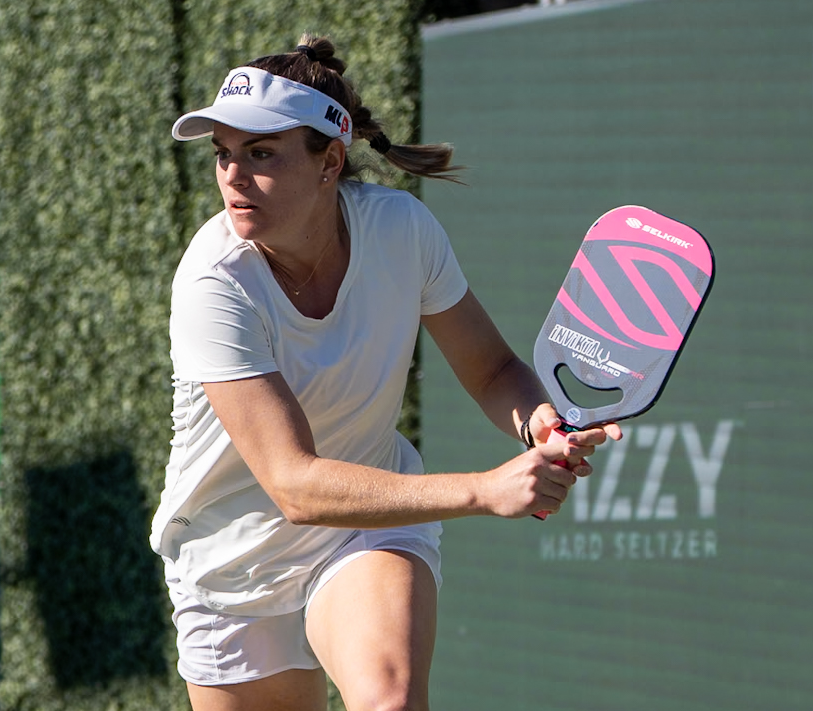 Judit Castillo playing pickleball with a paddle, wearing a white outfit and visor