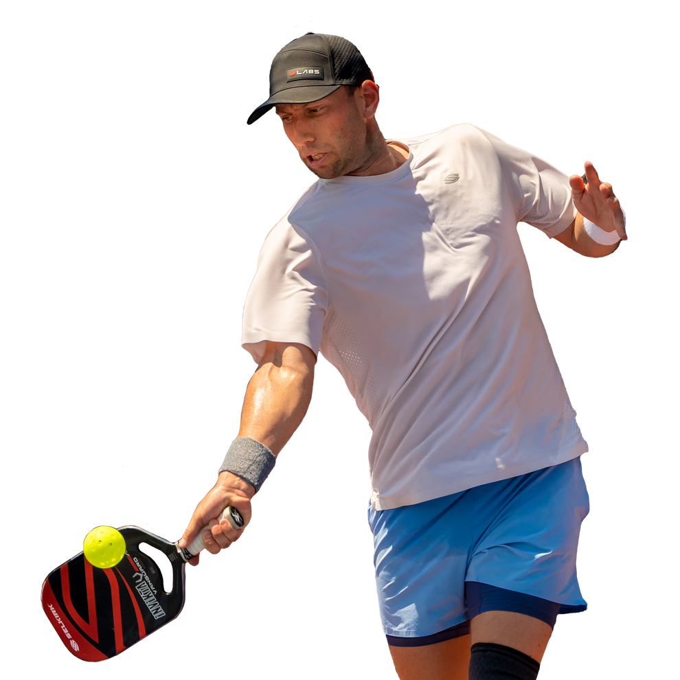 Male athlete swinging a Selkirk pickleball paddle to hit a yellow perforated ball.