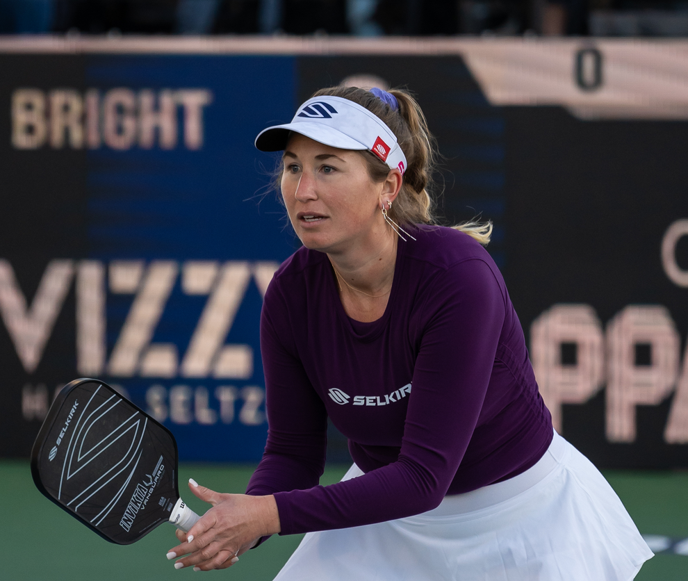 Lauren Stratman preparing to serve in a pickleball match, wearing a purple shirt and white skirt.