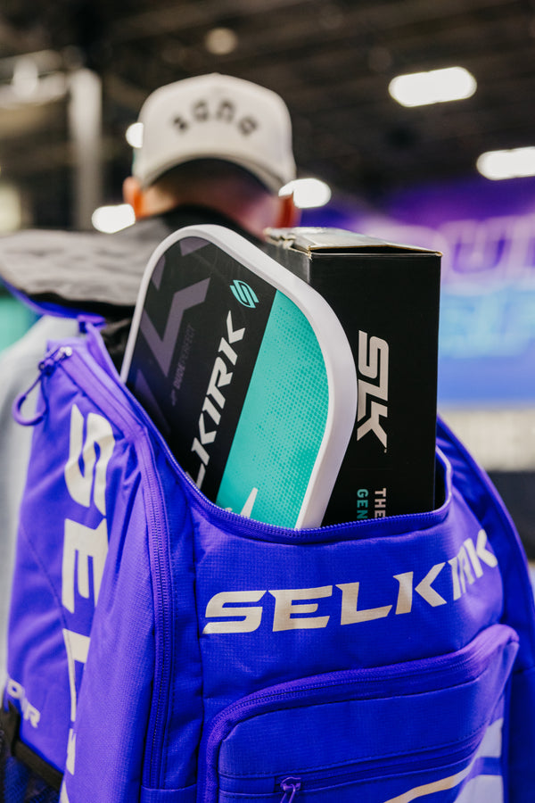 A close-up of a blue SLK backpack with a pickleball paddle and box partially visible inside.