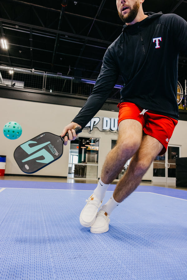 A player demonstrating a pickleball shot with the SLK by Selkirk x Dude Perfect Trickshot paddle.