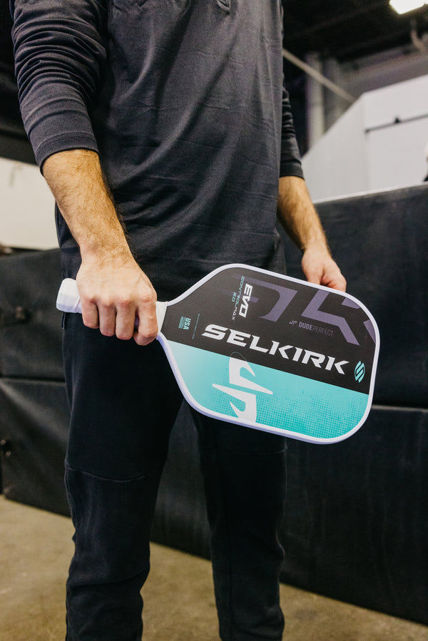 A person holding the SLK by Selkirk x Dude Perfect Evo 2.0 Control Max pickleball paddle, showcasing its design and grip.