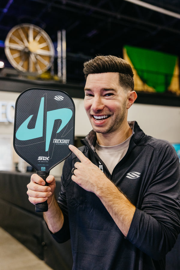 Man smiling and pointing at SLK x Dude Perfect Trickshot Pickleball Paddle with logo