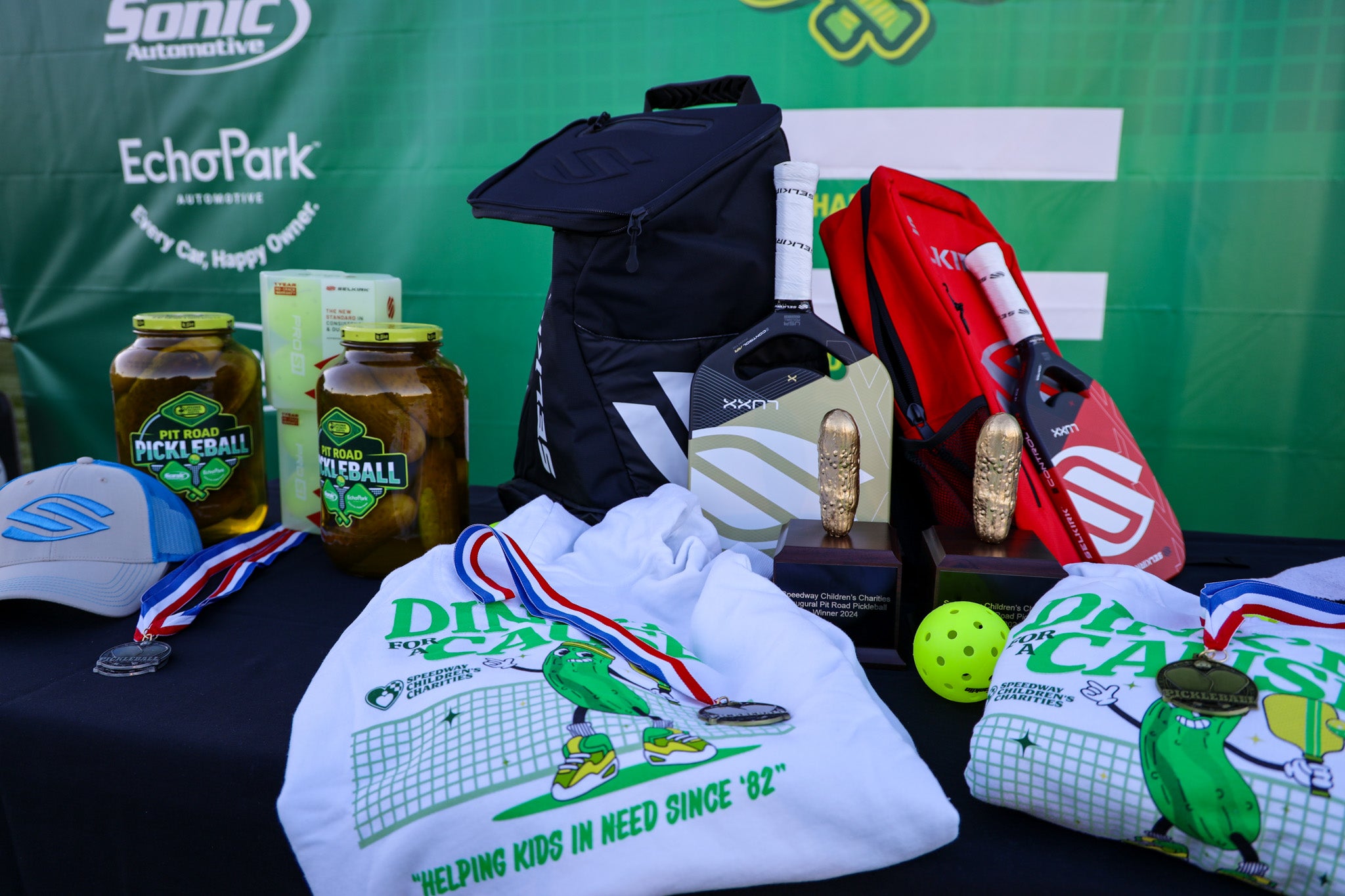 Display of pickleball equipment and prizes on a table, including paddles, balls, and medals.