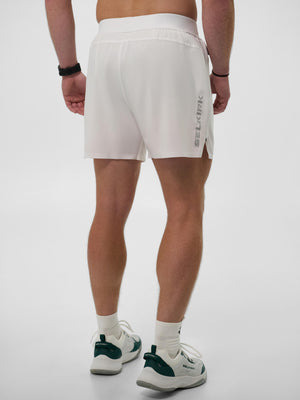 Rear view of a man wearing white SELKIRK athletic shorts and white sneakers with green accents.