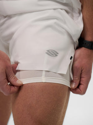 Close-up of hands adjusting white running shorts with inner mesh liner, reflective logo on outer thigh; wristwatch visible.