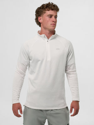 Male model wearing white textured long-sleeve quarter-zip pullover and light gray shorts, standing with hands at sides.