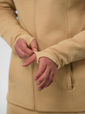 Close-up of a beige men's full zip jacket sleeve showing a thumb hole detail and a zippered pocket.