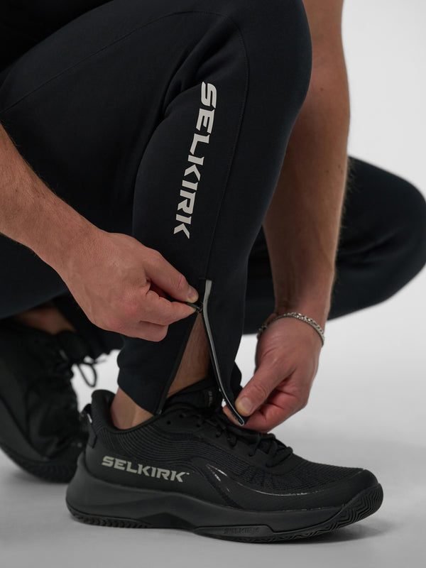 Man adjusting zippered ankle of Selkirk Pro Line Knit Jogger, showing logo on pants and shoes.