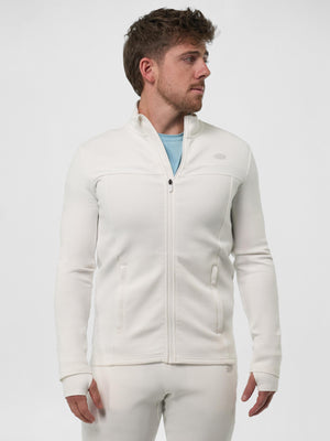 Male model wearing ivory full-zip athletic jacket with side pockets, light blue tee visible, matching ivory joggers, looking right.