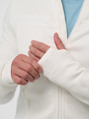 Hands adjusting thumb-hole cuff of a white zip-up jacket, light-blue shirt visible underneath.