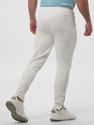 Back view of person wearing off-white jogger pants with ankle zipper and white SELKIRK sneakers; SELKIRK printed on pant leg.