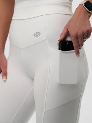 Close-up of white high-waist leggings showing a side pocket holding a black smartphone and a hand wearing a smartwatch.