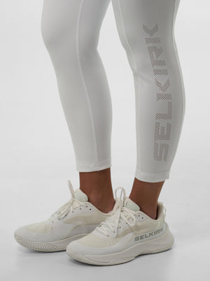 Cropped lower legs in light gray leggings with perforated SELKIRK on calf and cream athletic shoes marked SELKIRK.