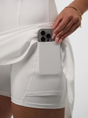 White athletic skort showing a side pocket holding a smartphone as a hand with gold bracelet slides the phone in