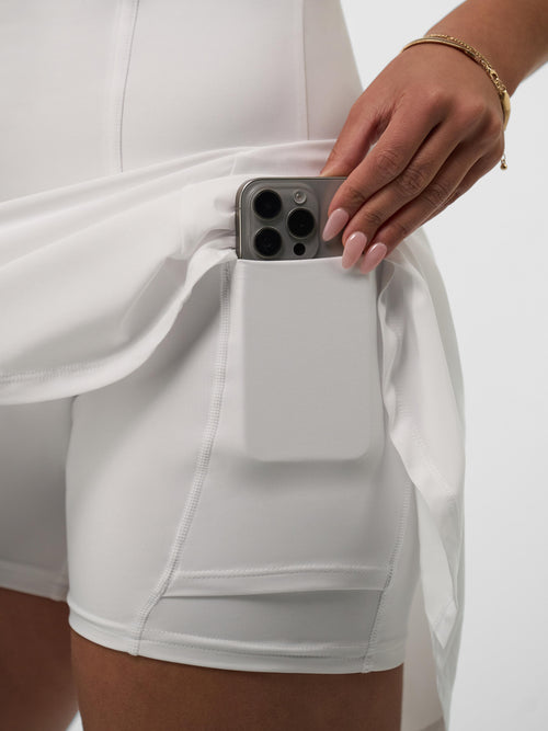 A woman placing a phone in the pocket of a white pickleball dress.