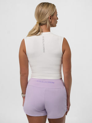 Woman viewed from back wearing a white sleeveless crop top and lavender shorts; SELKIRK printed on the top and waistband.