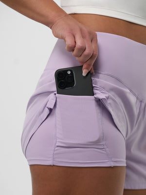 Hand sliding a smartphone into the side pocket of lavender athletic shorts.
