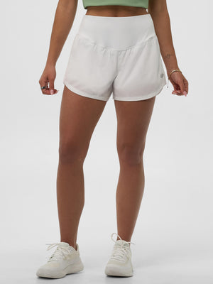 Women's white high-waist athletic shorts on model, mid-thigh length with curved hem and small reflective logo on left leg