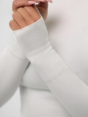 White long-sleeve top cuff with thumbhole and a manicured hand with nude-pink nails