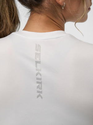 Back view of a woman wearing a white shirt with vertical SELKIRK logo between her shoulder blades.
