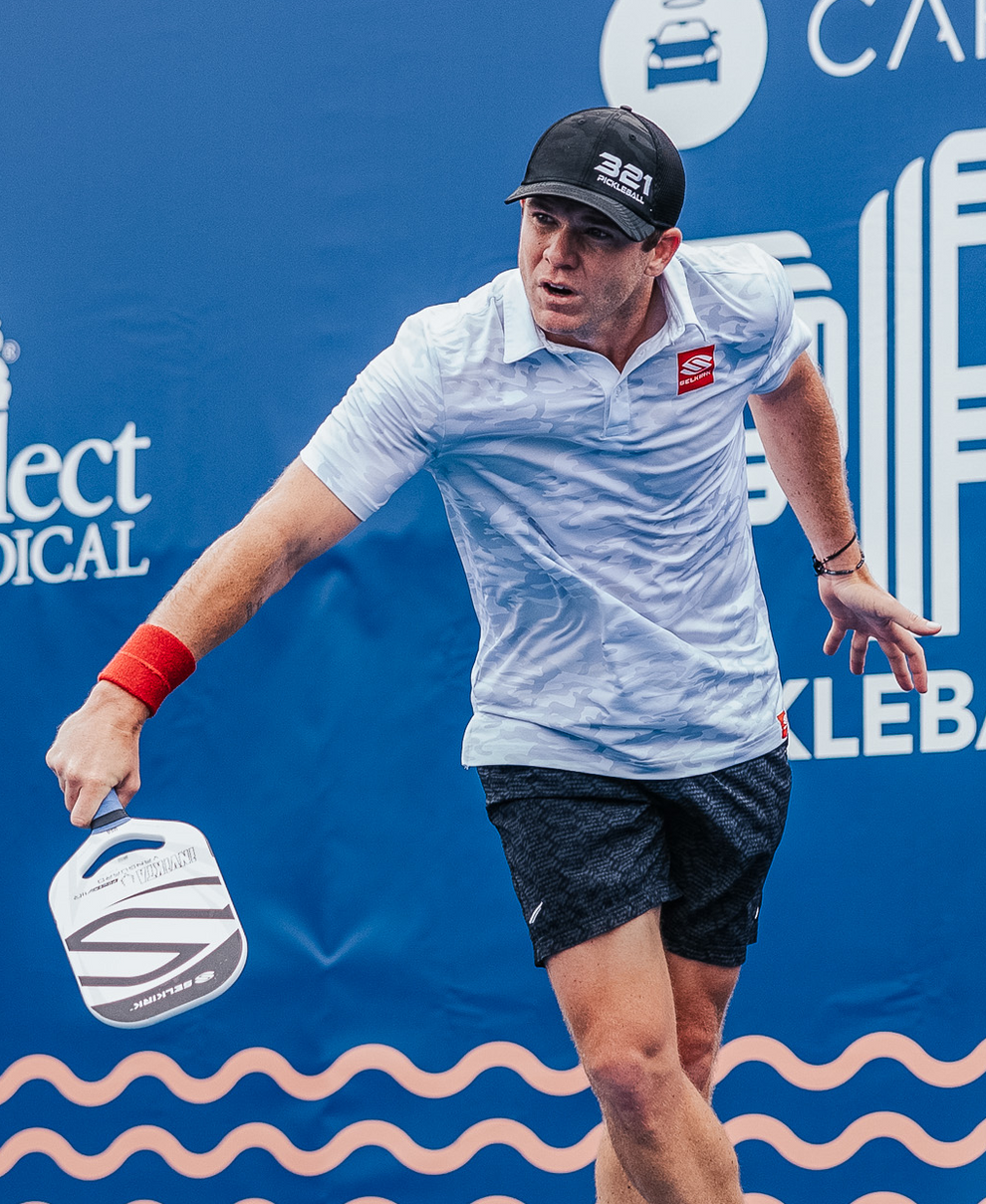 Rob Nunnery serving with a pickleball paddle on a blue background