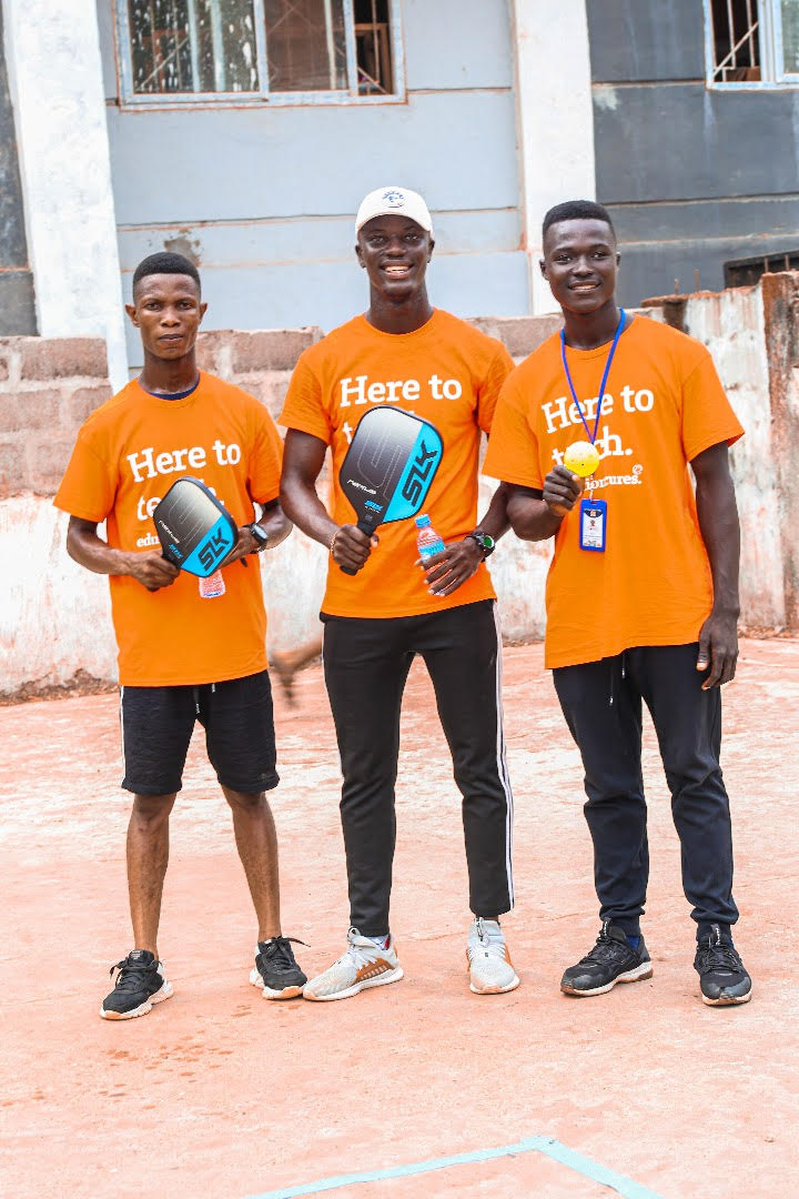 Three men stand shoulder to shoulder and smile at the camera as they hold up their SLK Nexus pickleball paddles and balls. 