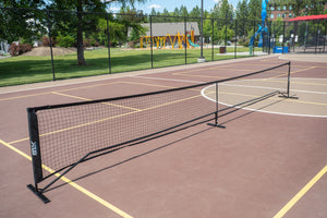 SLK Pro Portable Pickleball Net set up on a court with a playground in the background.