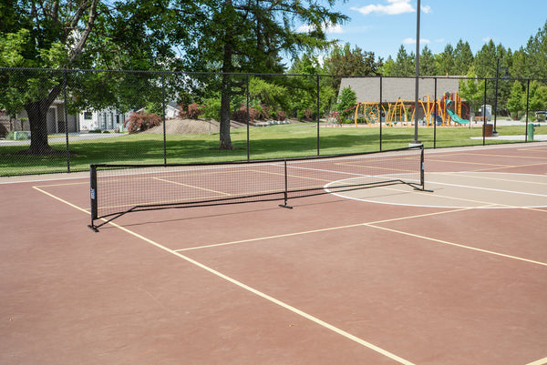 SLK Pro Portable Pickleball Net set up on a court with playground in the background