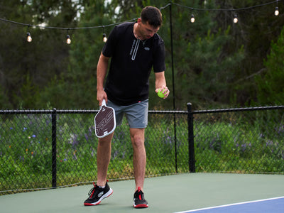 A player preparing to serve with the SLK HALO Pro - Max pickleball paddle in blue on a court.