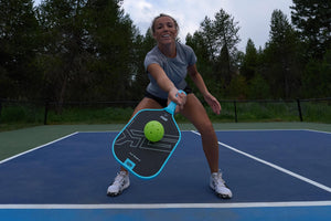 A player reaching for a pickleball with the SLK HALO Control paddle on a court.