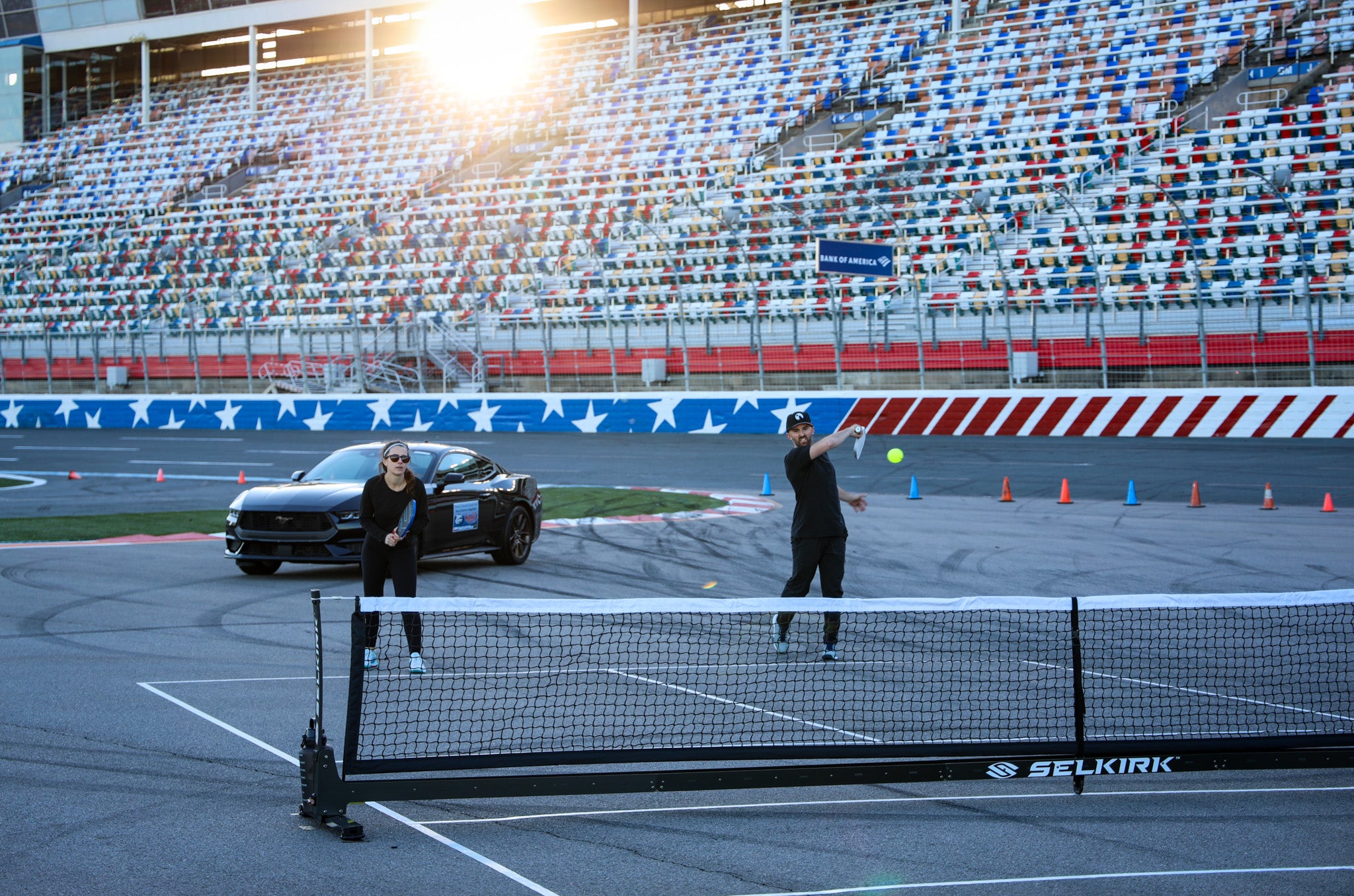 NASCAR drivers playing pickleball on a racetrack with a car in the background