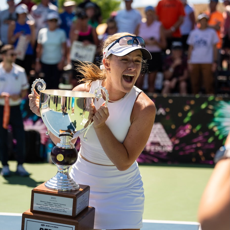 A player celebrating with a trophy after winning a pickleball match.