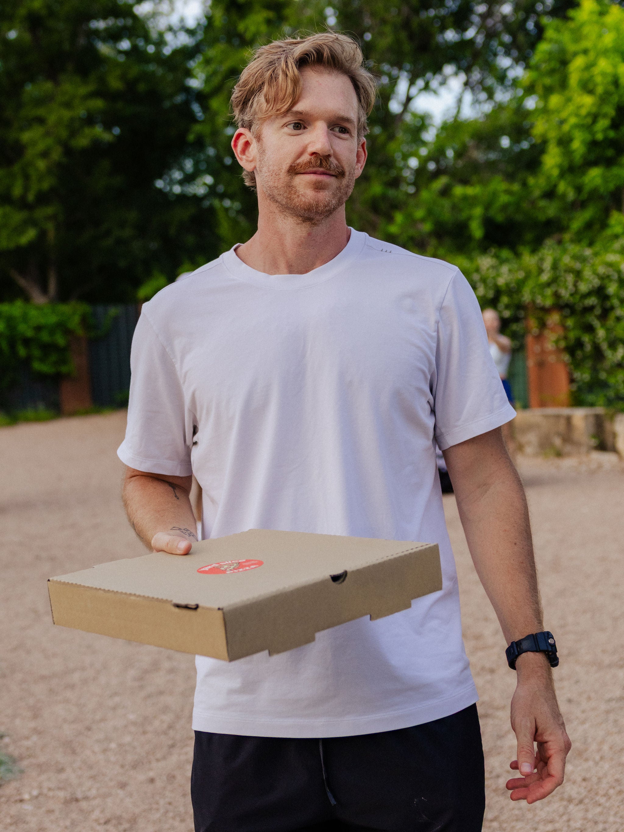 A man smiles as he holds a cardboard pizza box. 