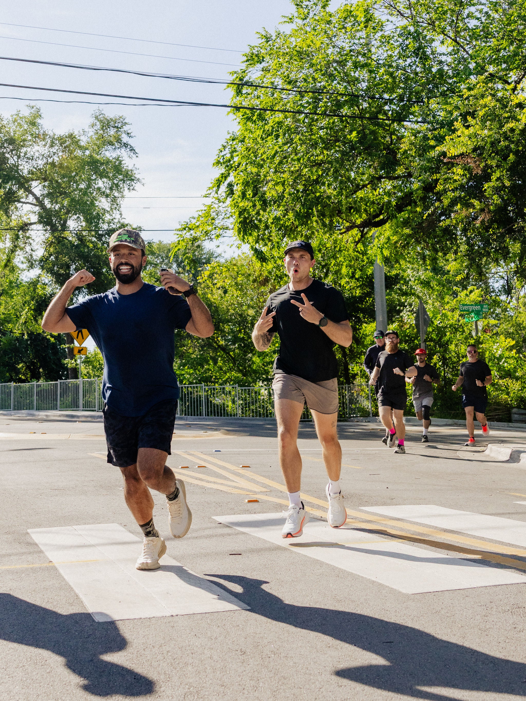 One man shows off his muscles while another olds up peace signs as they run outside. 