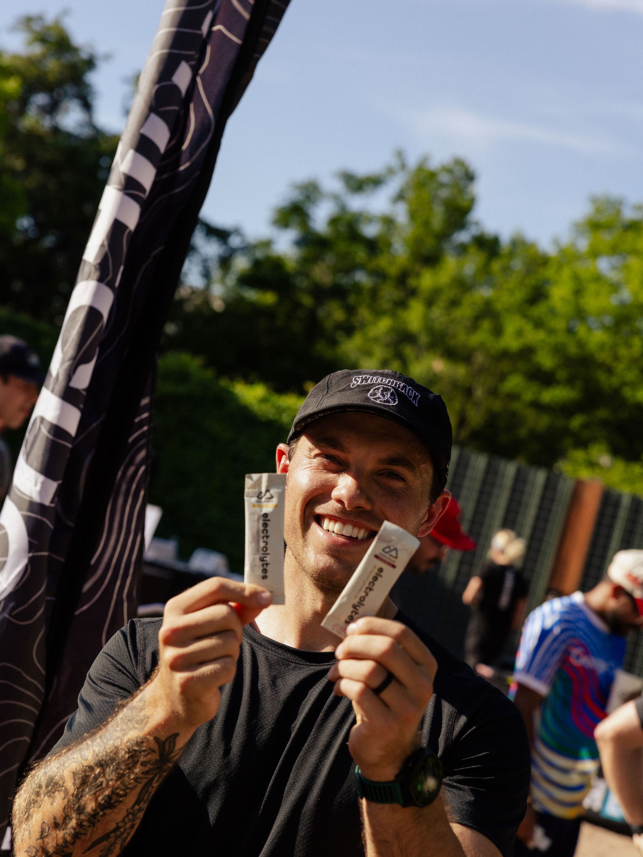 A man smiles as he holds up two packets of Switchback electrolytes. 