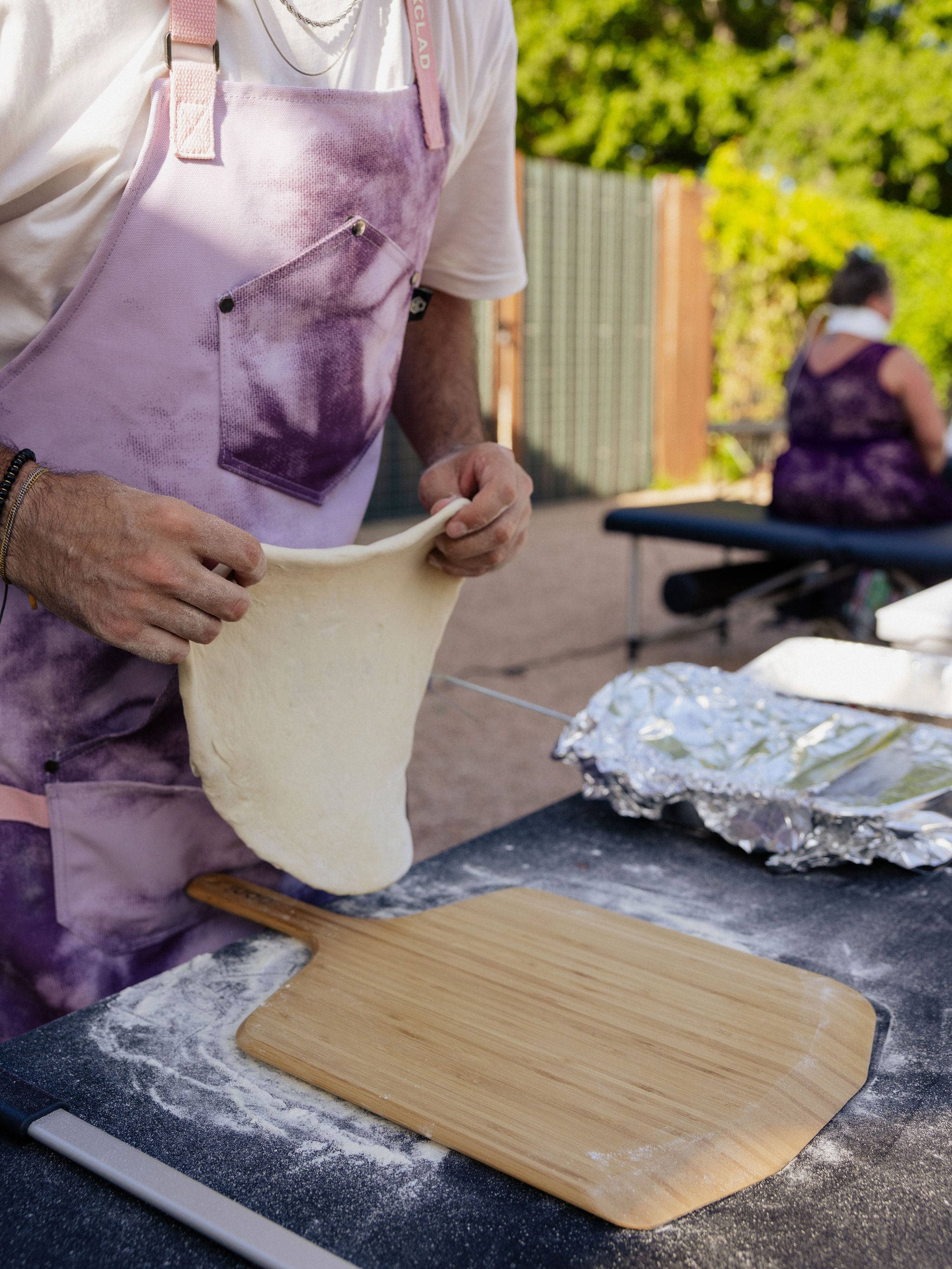 A close-up shot shows a man preparing pizza dough on a wooden pizza paddle. 