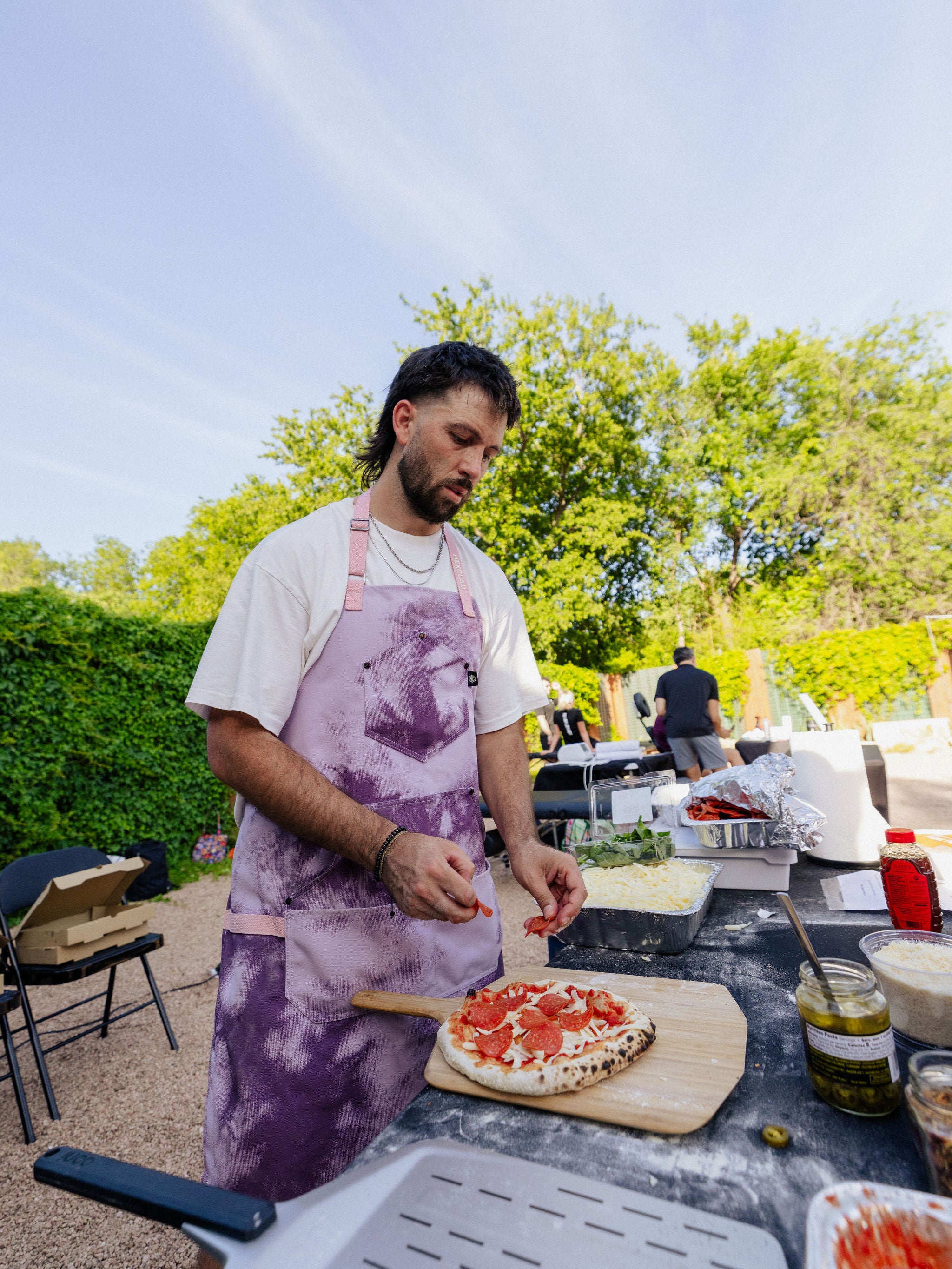 A man adds pepperoni to a hand-tossed pizza that rests on a wooden pizza paddle. 
