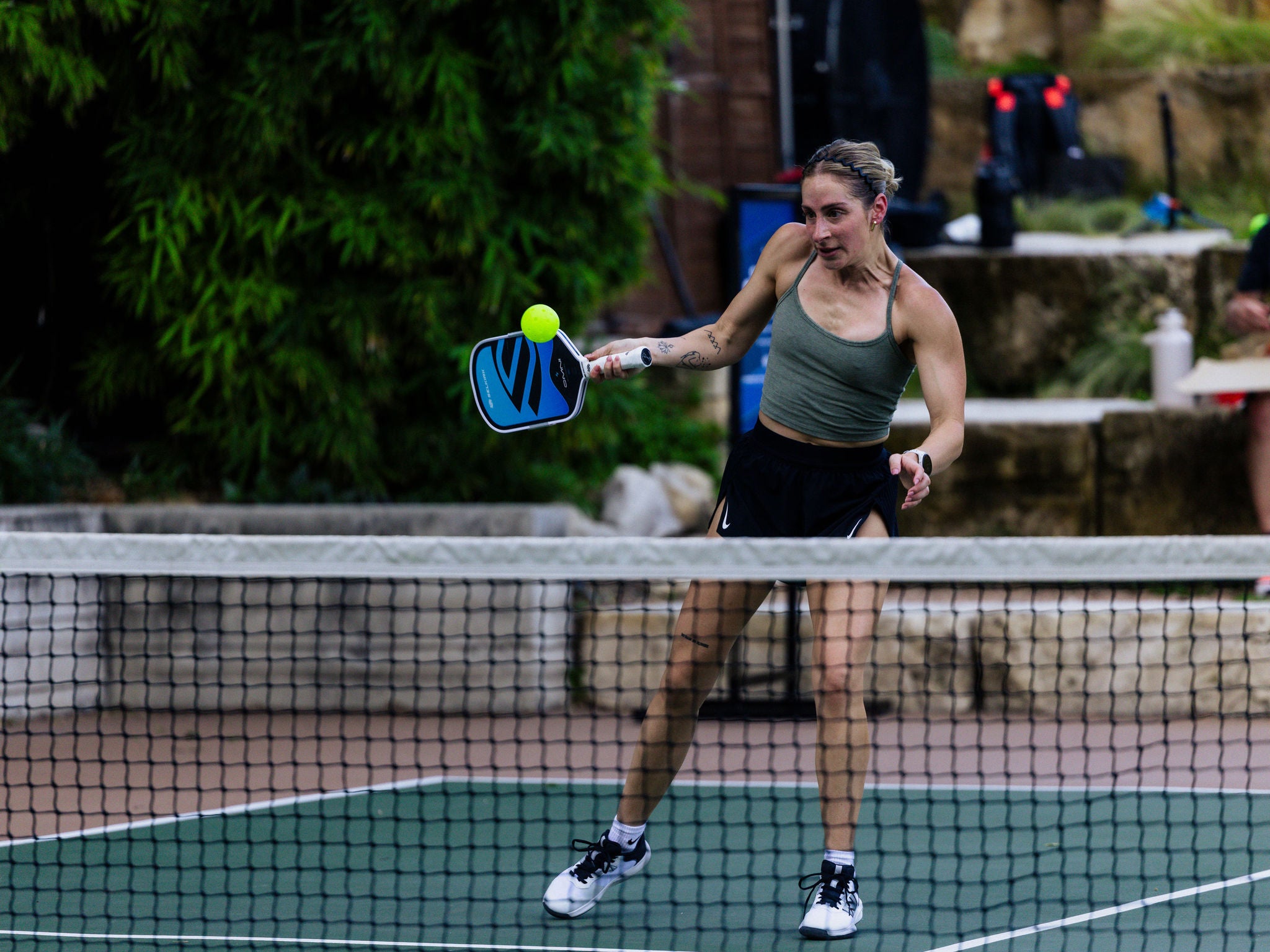 A woman hits a volley shot with her Selkirk OMNI paddle on an outdoor pickleball court. 