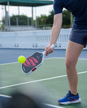 Black Boomstik paddle making contact with a pickleball