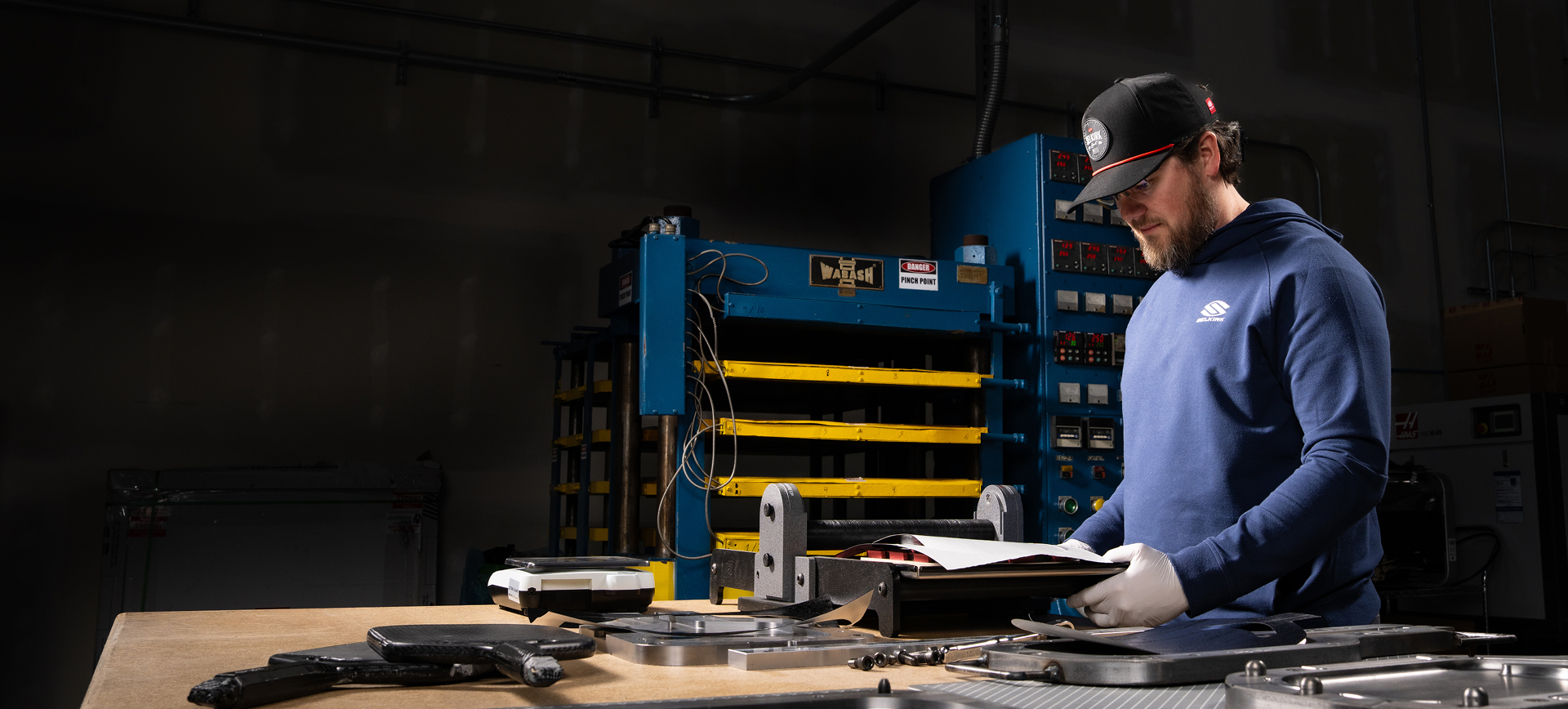 Selkirk Sport technician in branded gear reviewing precision paddle materials at a high-tech manufacturing station, surrounded by molds and composite layers under focused workshop lighting.