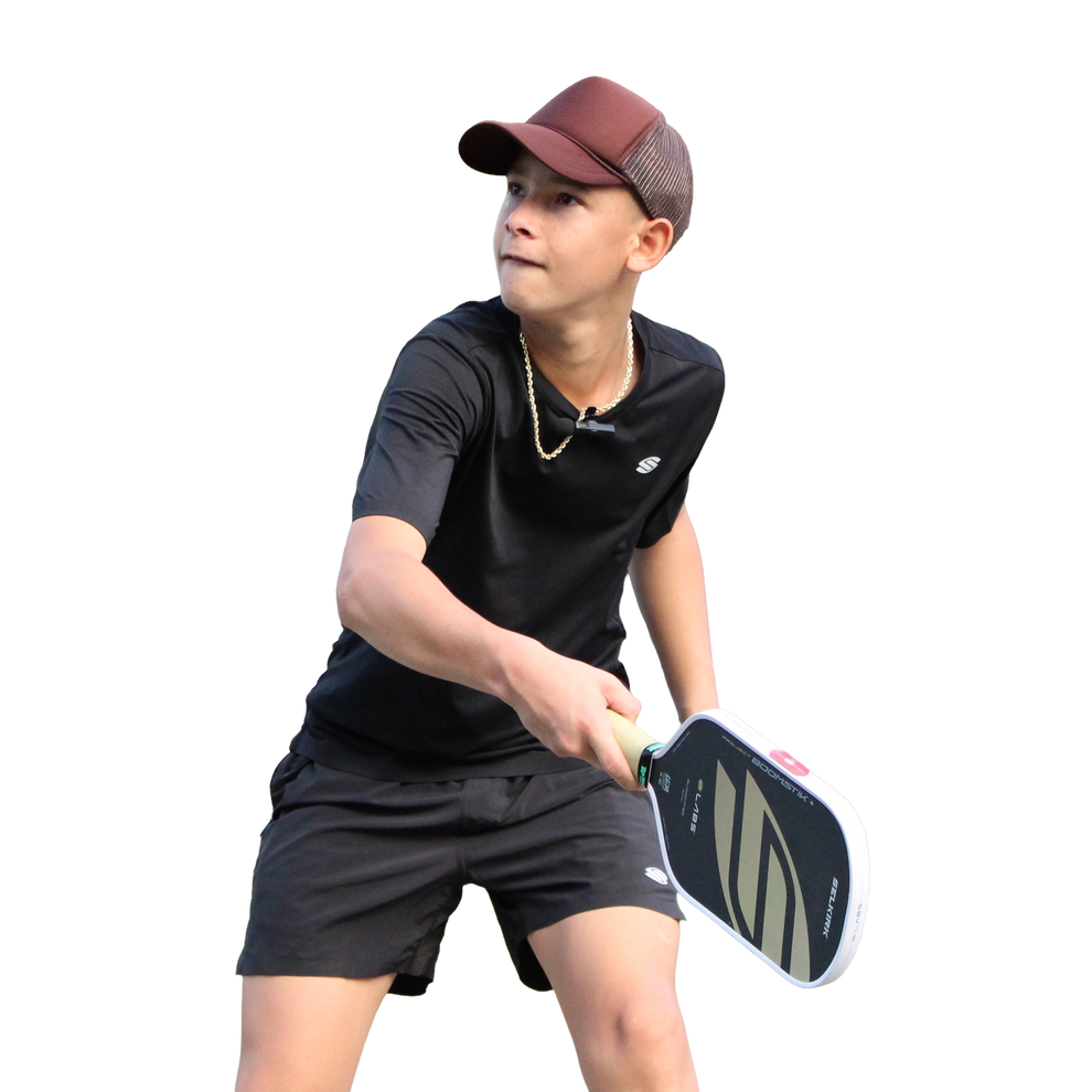 Teen wearing maroon cap and black athletic clothes poised to hit a pickleball paddle